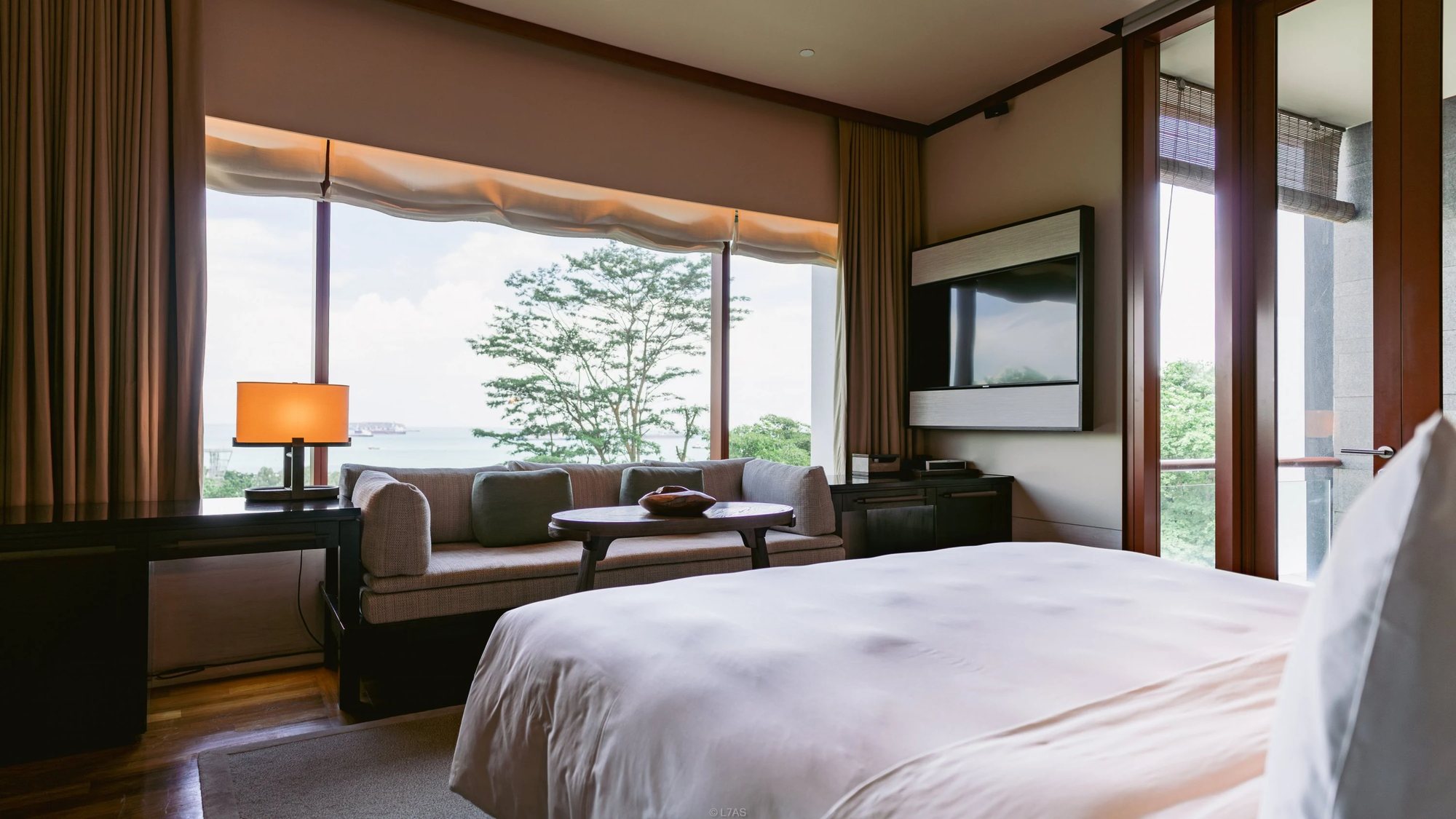 A Premier Seaview Room with a king bed, a sofa and a wide window over trees and the sea