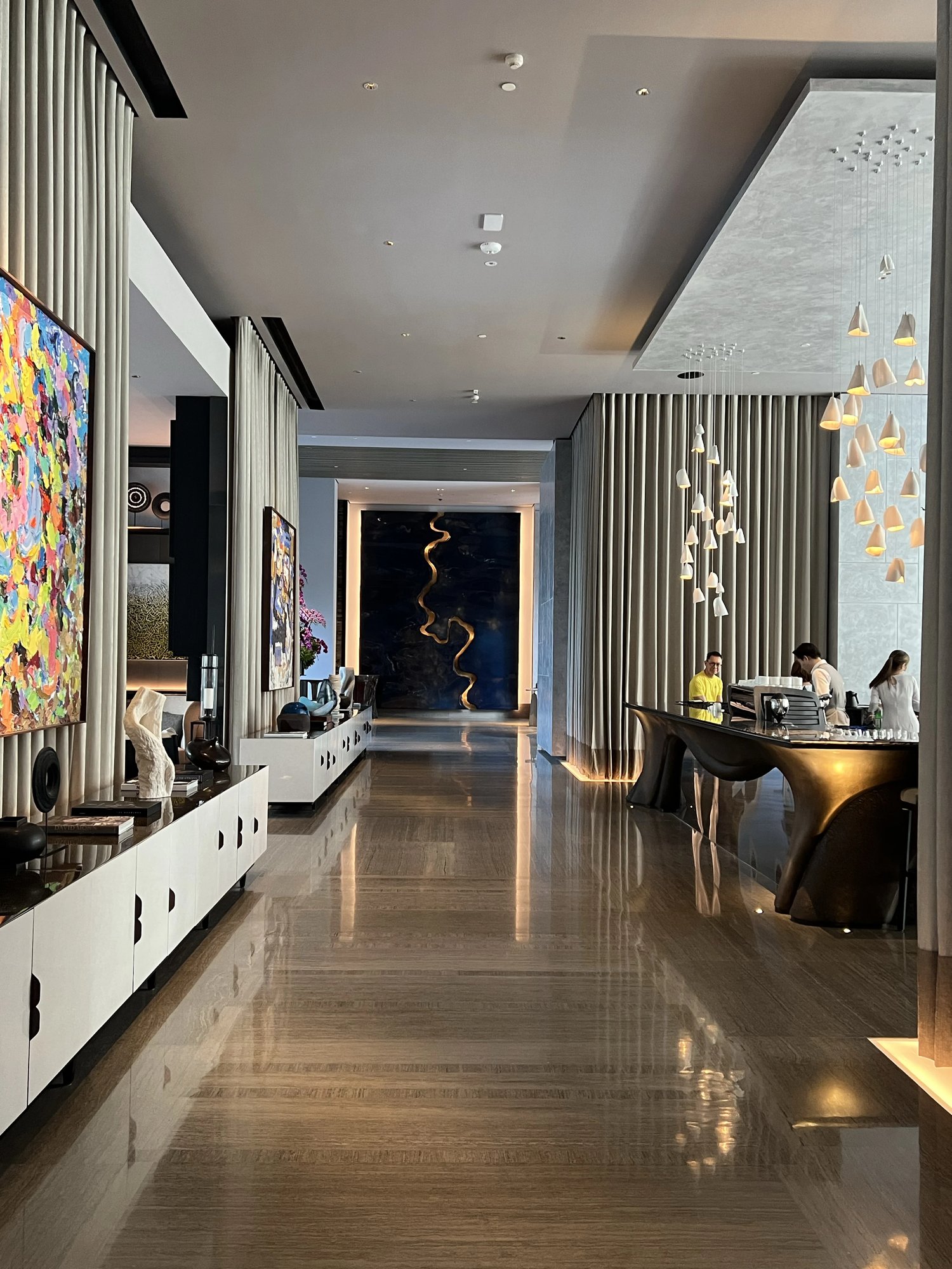 The long marble lobby gallery with bright art on one side and the front desk beyond