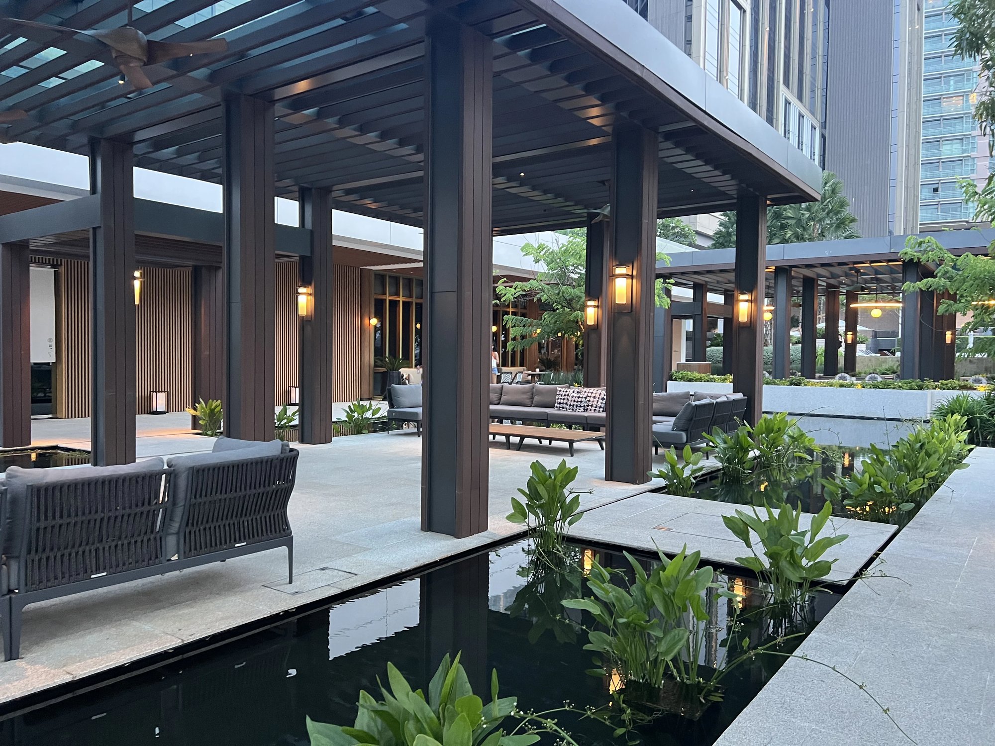 A timber pergola terrace beside the lit pond at dusk
