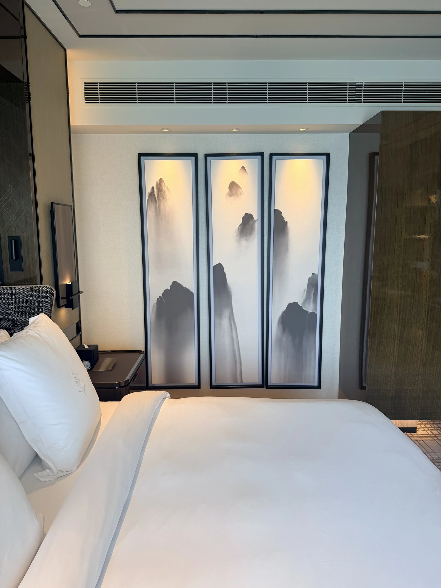 The bed beneath a triptych of ink paintings