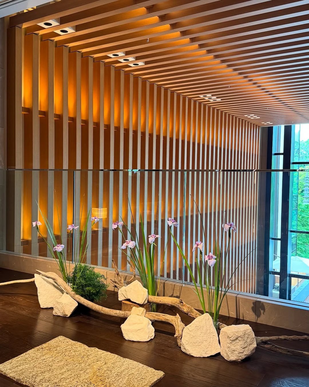 The amber slatted wall of the lobby with iris ikebana