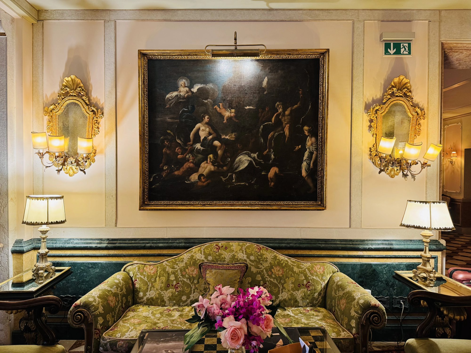 A salon sofa under an old master painting and gilt sconces
