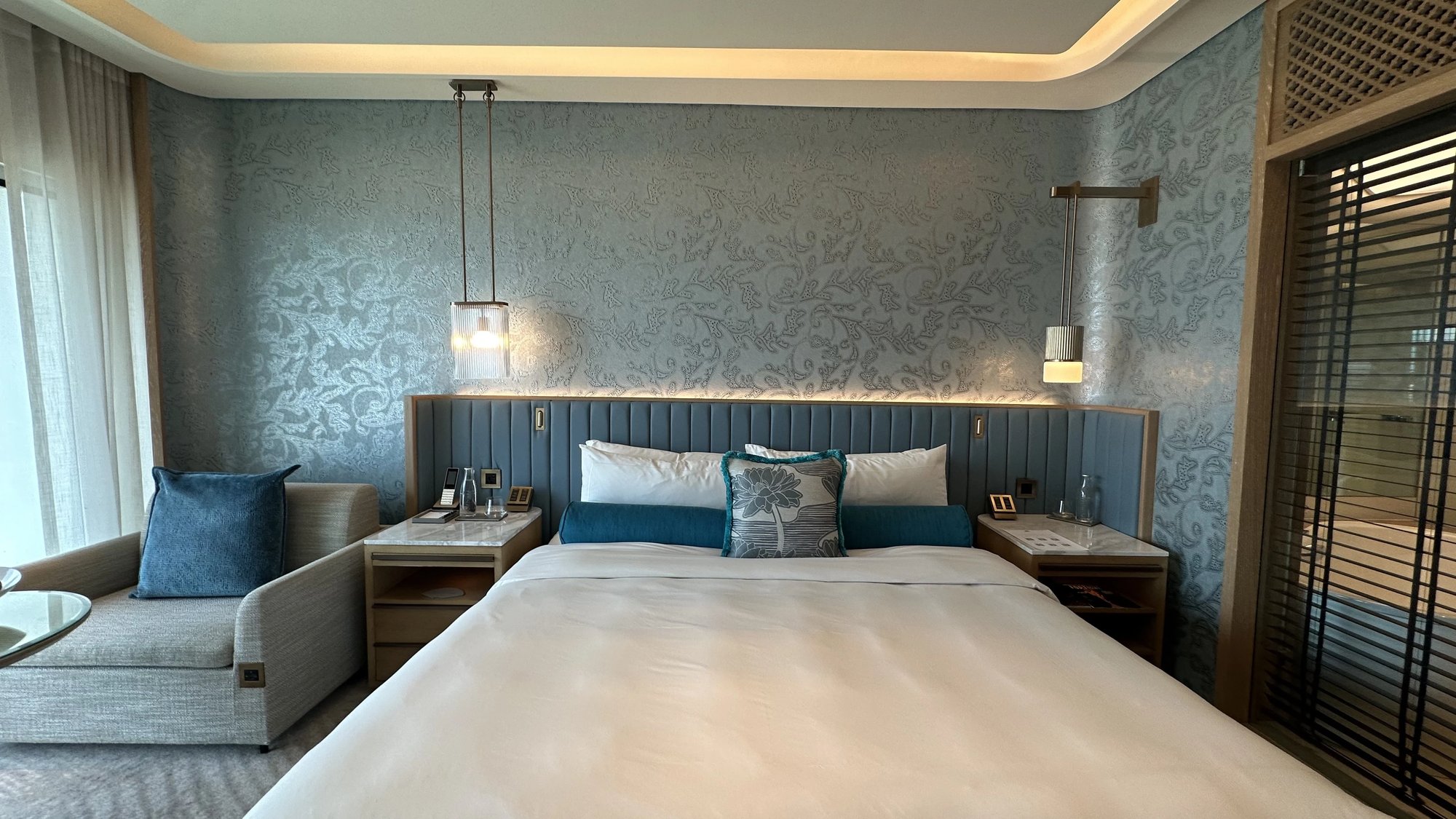 The bed with a blue panelled headboard and patterned wallpaper