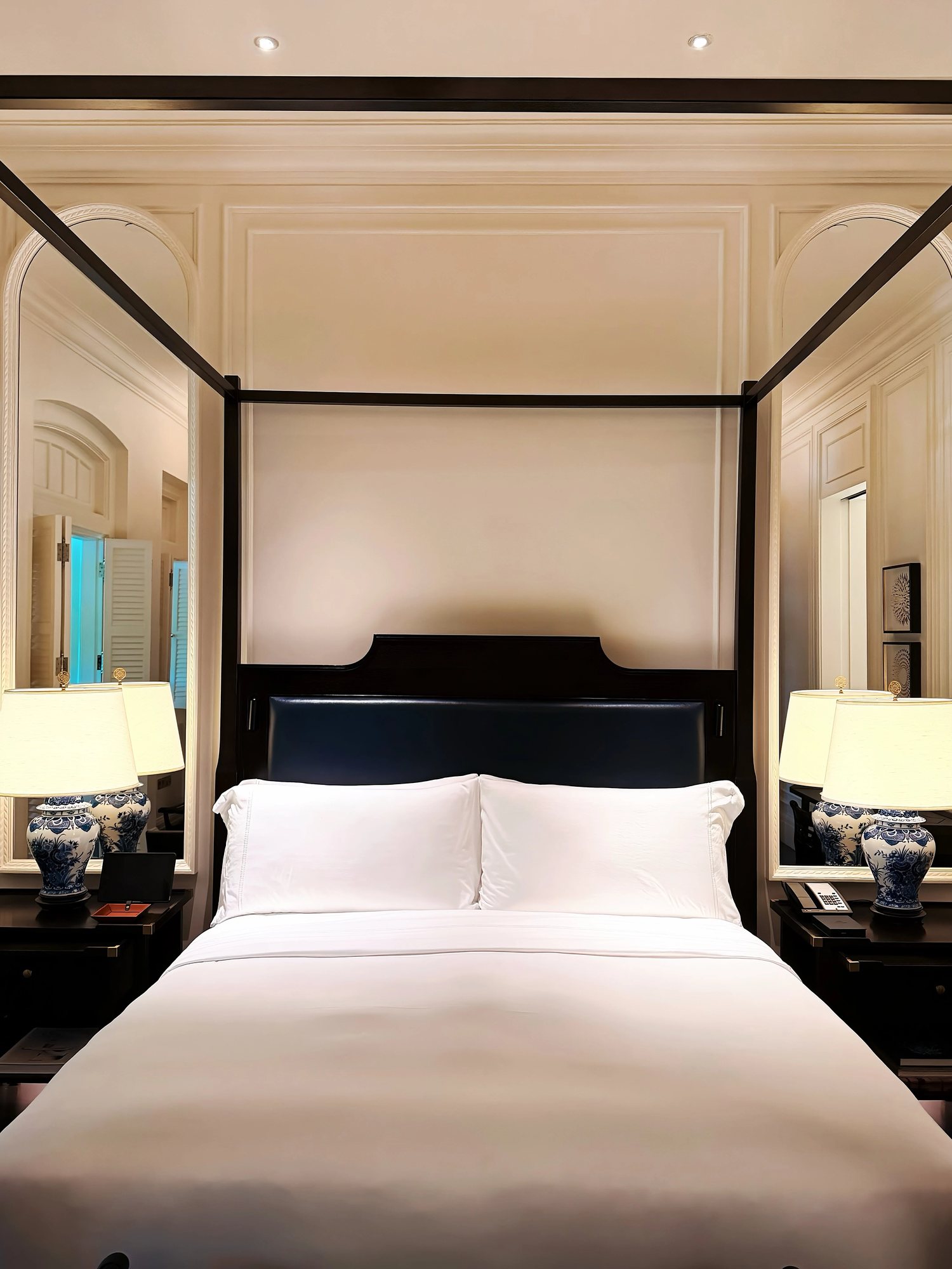 A four-poster bed with white linen and blue-and-white lamps in a Raffles suite