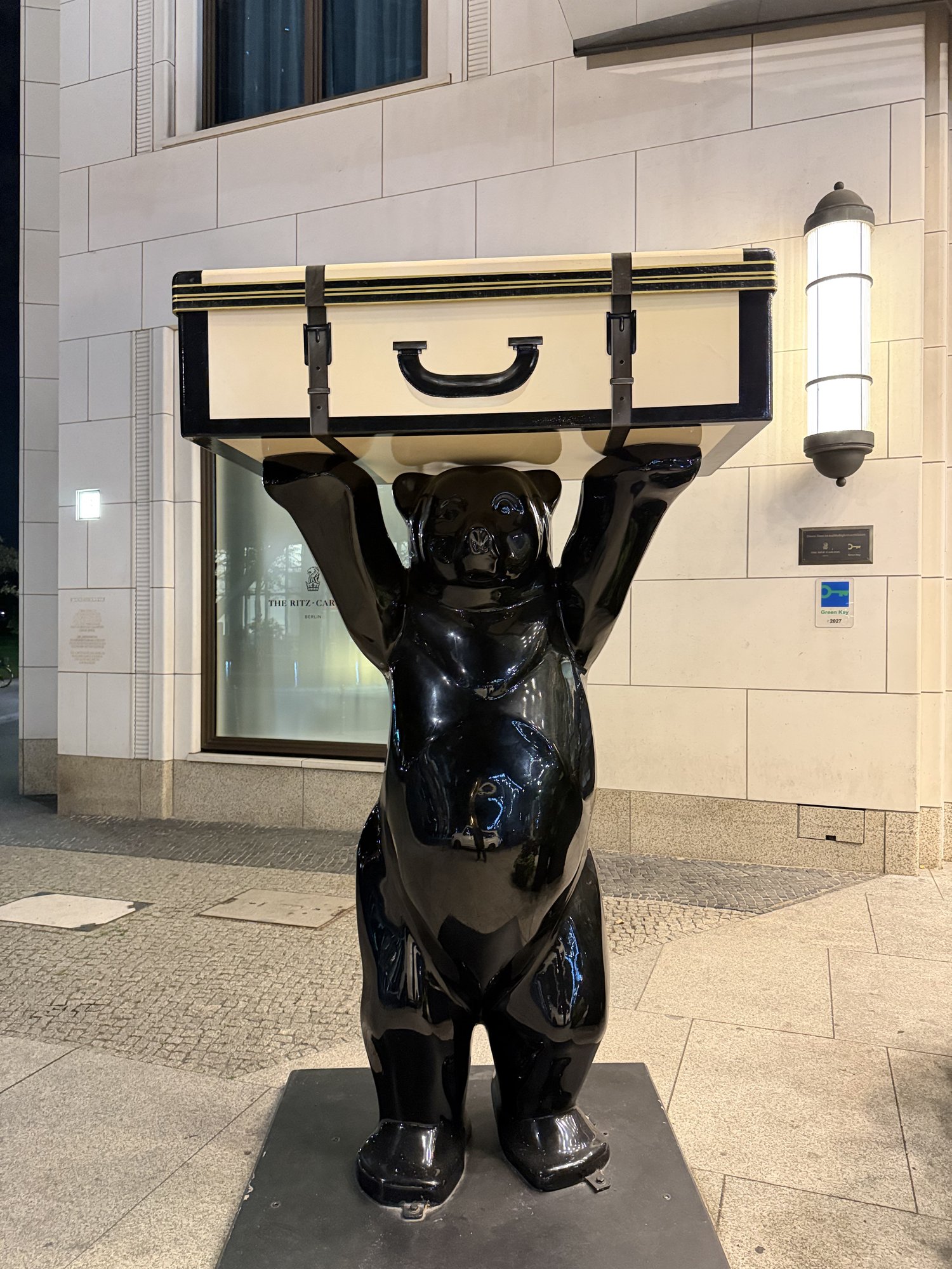 A black Berlin bear statue holding a suitcase by the door