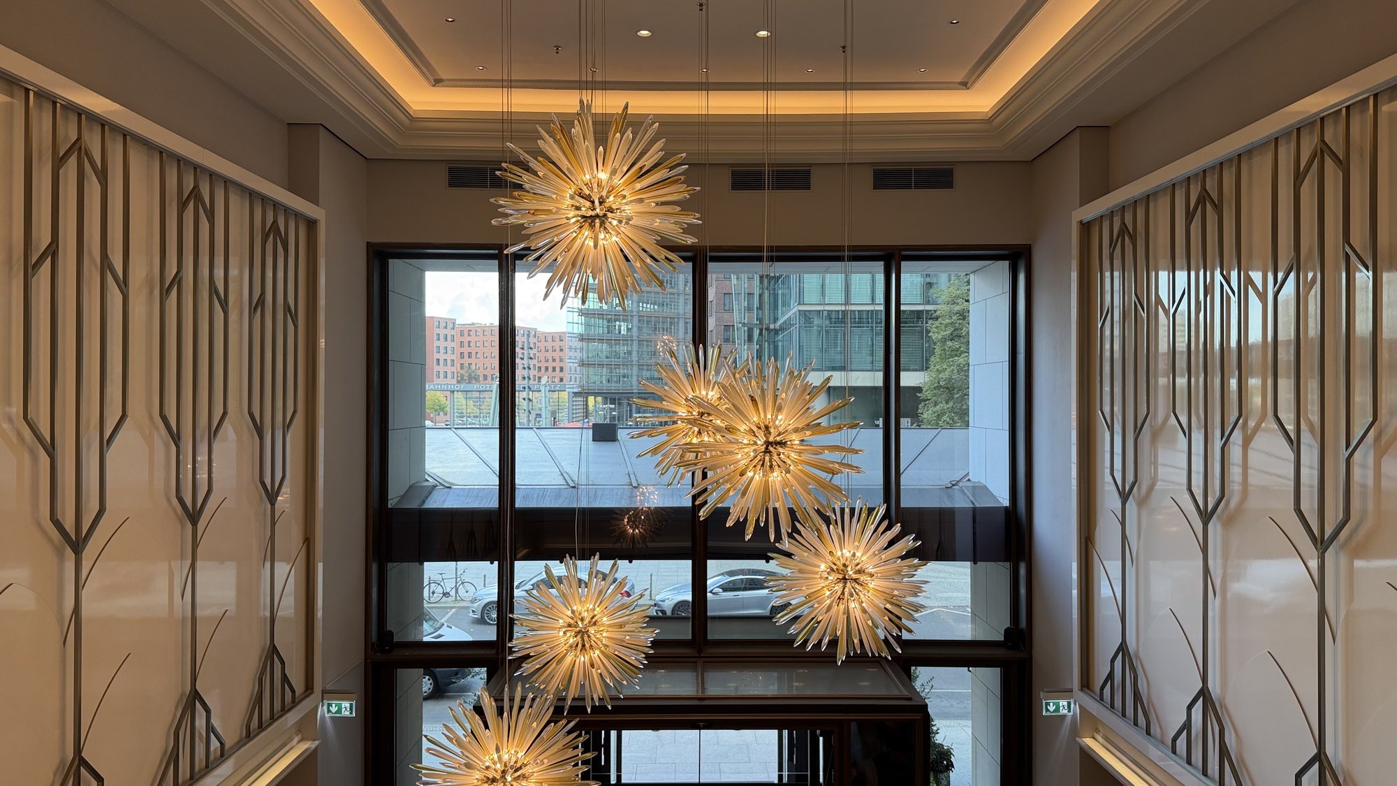 Starburst chandeliers hanging by a tall lobby window