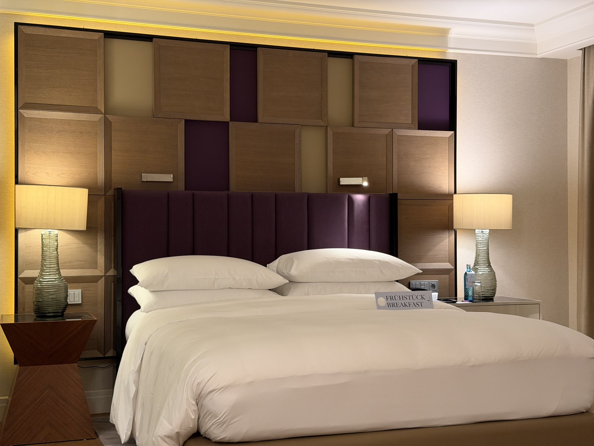 The bed and purple channelled headboard with green glass lamps
