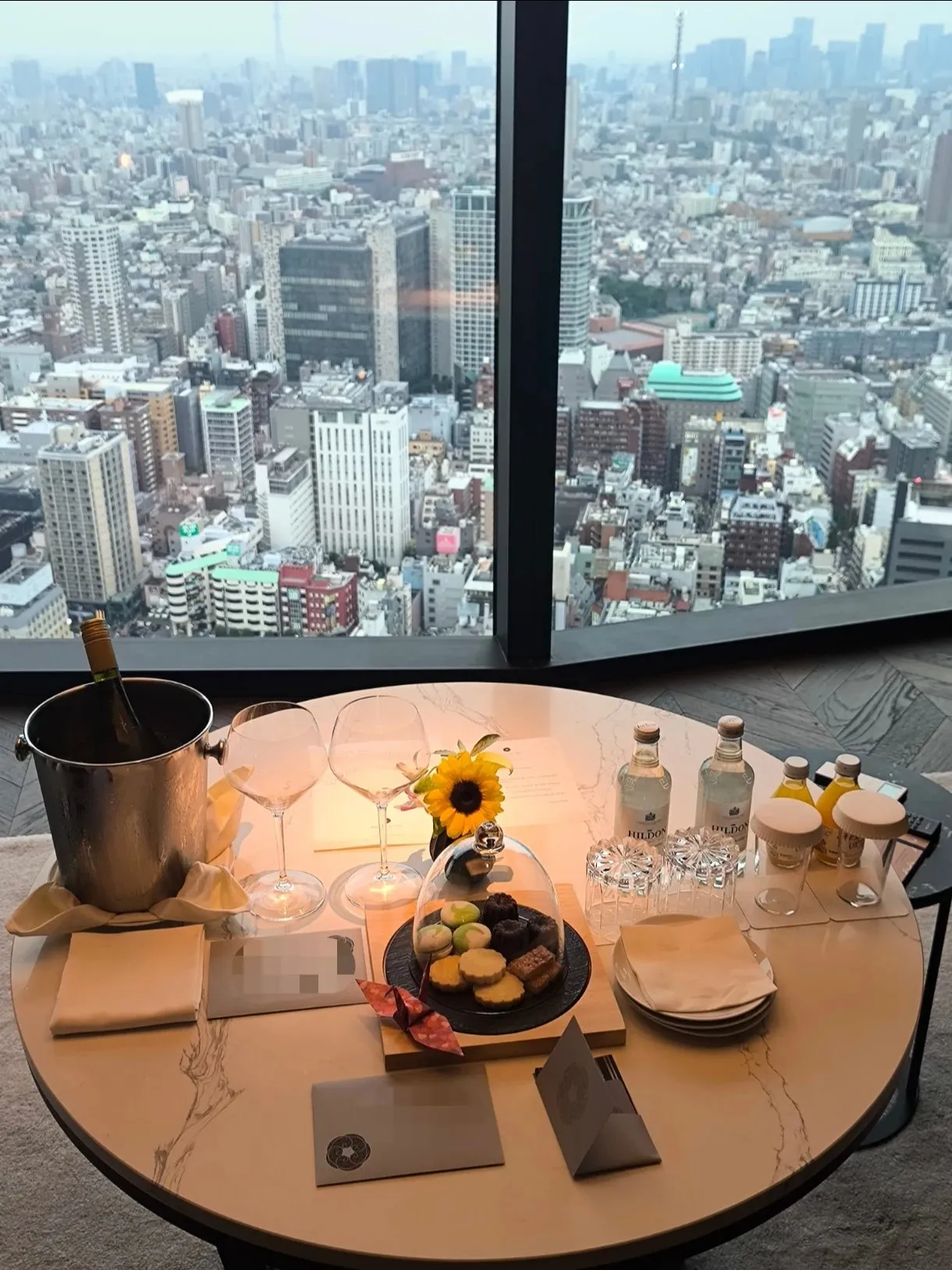 A welcome table by the corner window with sweets and a champagne bucket above the city