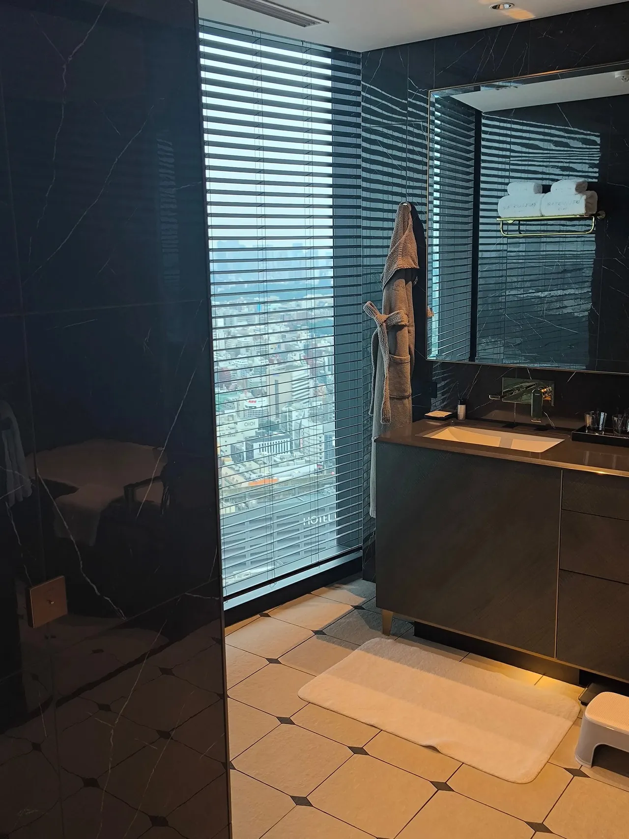 The bathroom vanity beside a tall window with blinds, on a pale tiled floor