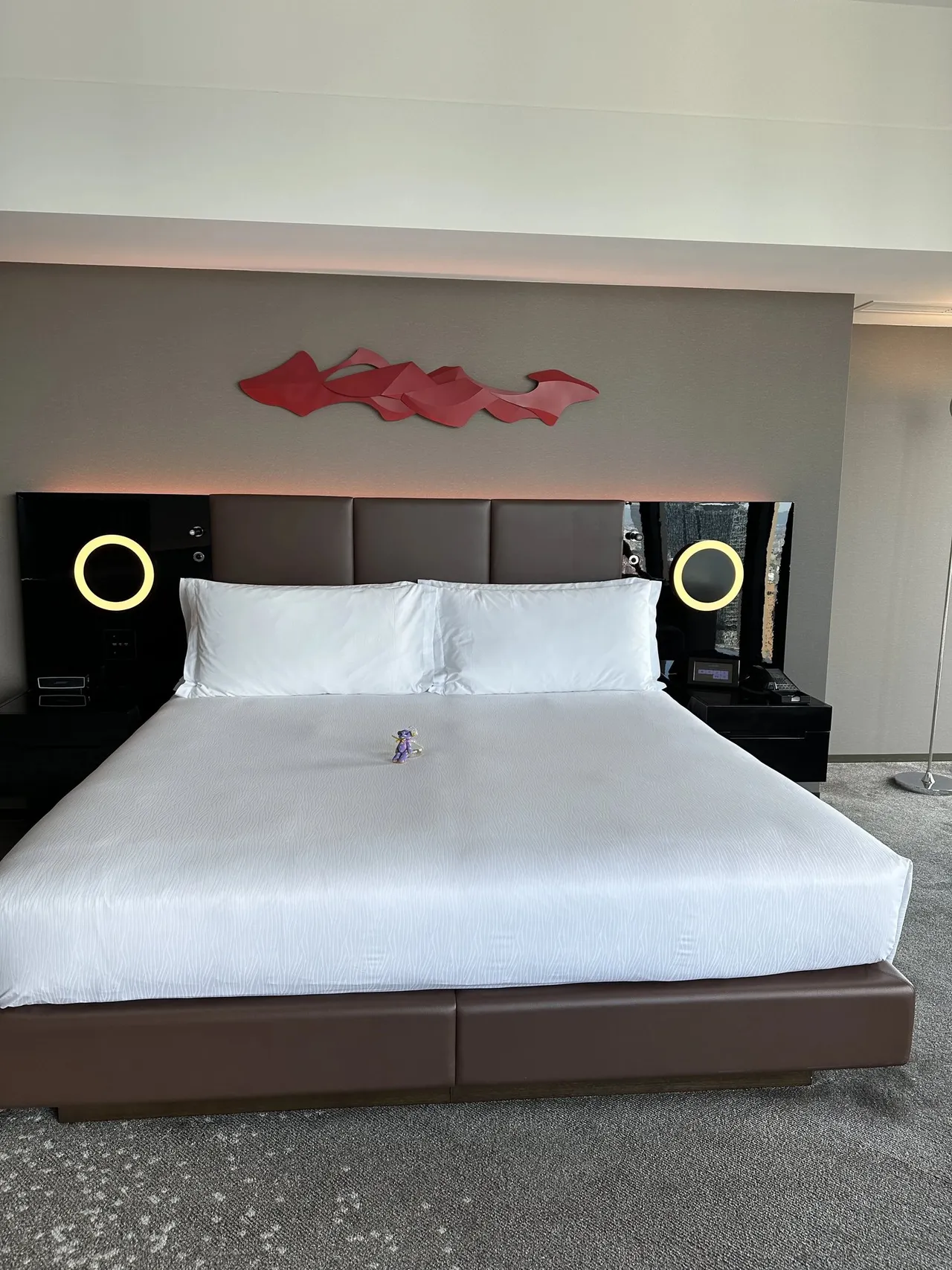 The wide king bed with white linen, a red wall sculpture and glowing ring lights in the Executive King Corner room on the 35th floor