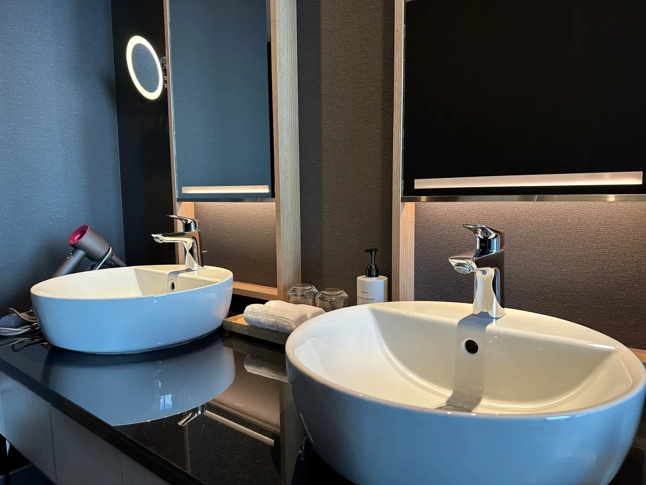 The double vanity with two white vessel basins and a lit round mirror