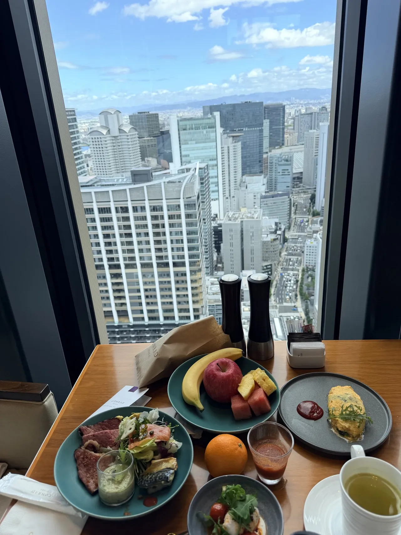 A breakfast table by the window with eggs, fruit and green tea above the skyline