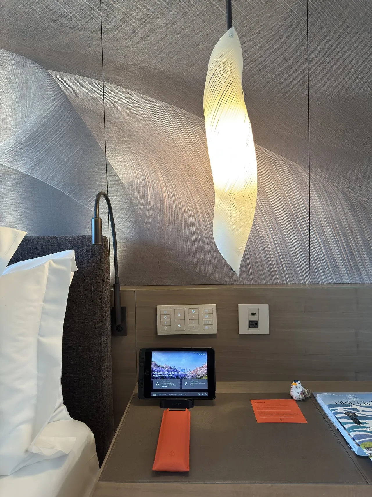 A feather-shaped pendant lamp and control tablet by the bed