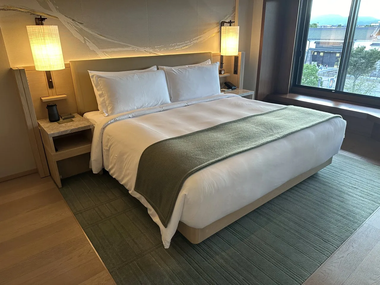 The king bed with a green runner and lamps beside the window