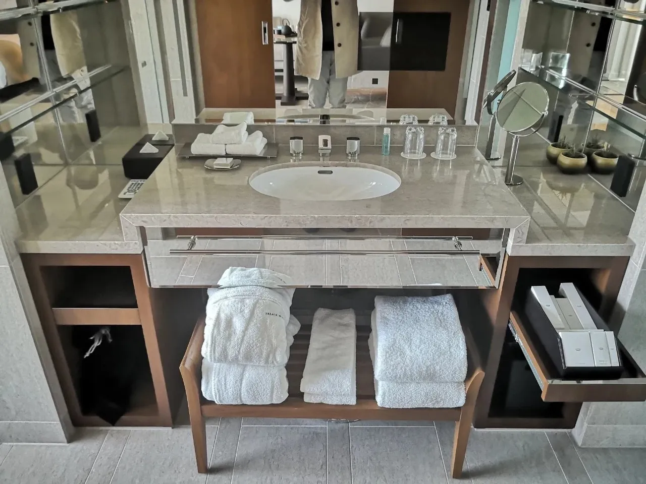 A single marble vanity with folded white robes and towels on the shelf below