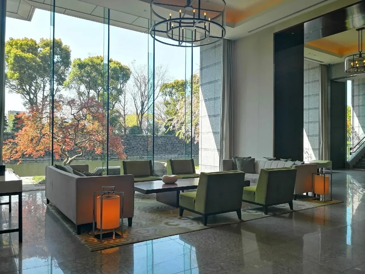 The lobby lounge with tall glass walls onto maple trees and the moat, green armchairs and lanterns