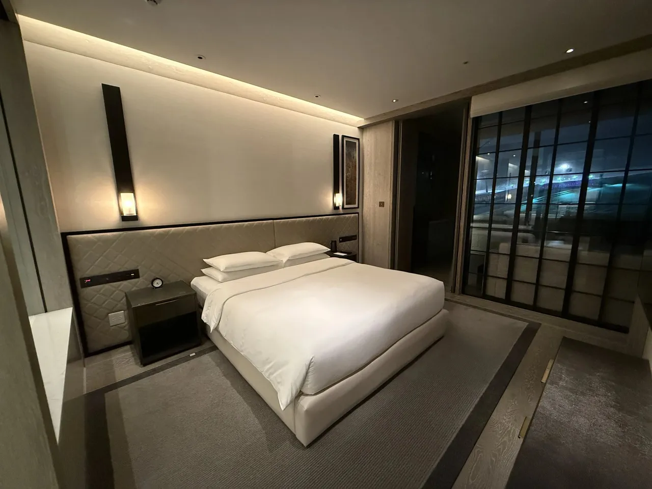 The suite bedroom, a wide white bed under a cove light beside black-framed windows
