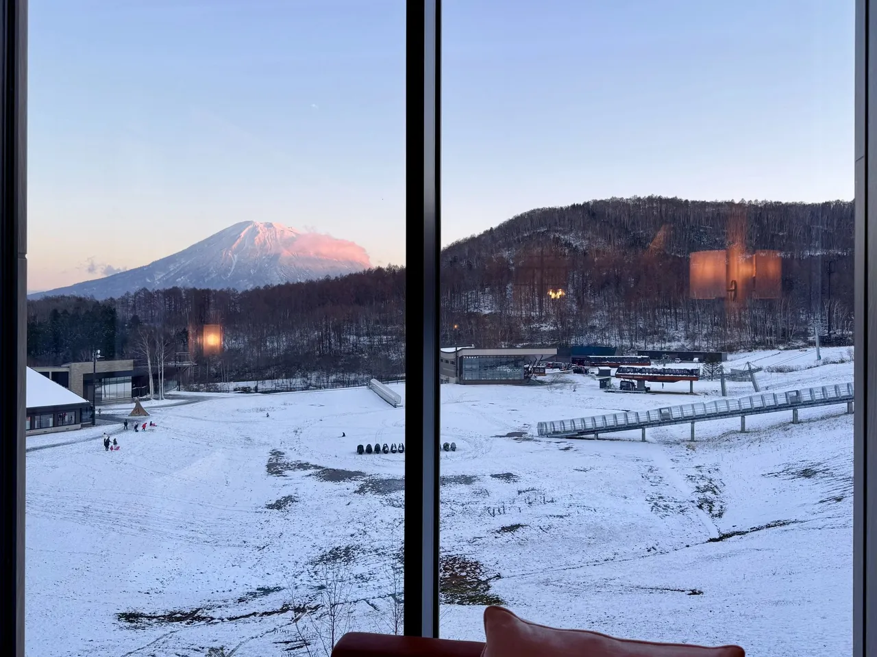 Mt Yotei glowing pink at sunrise over a snowy field, seen through the window