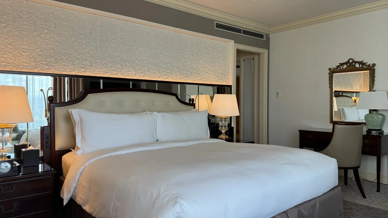 Bed with a pale quilted headboard, carved wall panel and a dressing table
