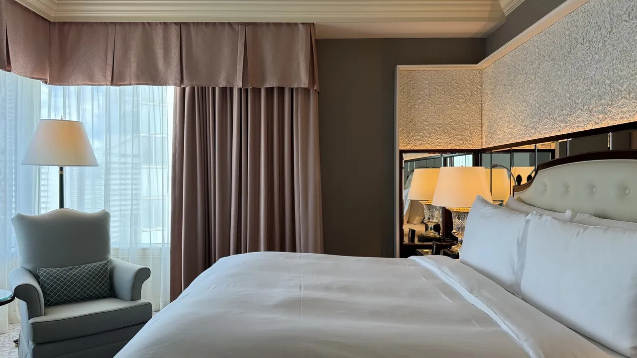 Bed and armchair beside a pink-curtained window
