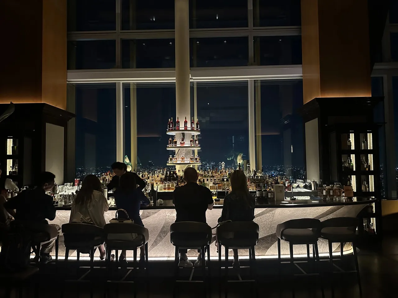 The bar counter and lit tower of bottles against the night windows
